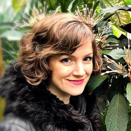 Headshot of Piper Reynolds, brunette white woman with a short bob against a green leafy background